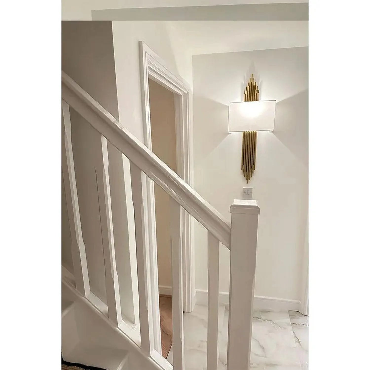 Gold vertical ribbed wall sconce with white shade mounted in modern stairwell hallway.
