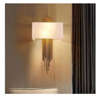 Modern gold wall sconce with rectangular cream shade and cascading metal rods, installed above upholstered headboard in warm 