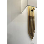 Gold fringe wall sconce with cascading metal rods mounted on white wall with white bracket arm.