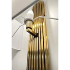 Gold ribbed wall sconce with white LED bulb installed, shown mounted on white wall.
