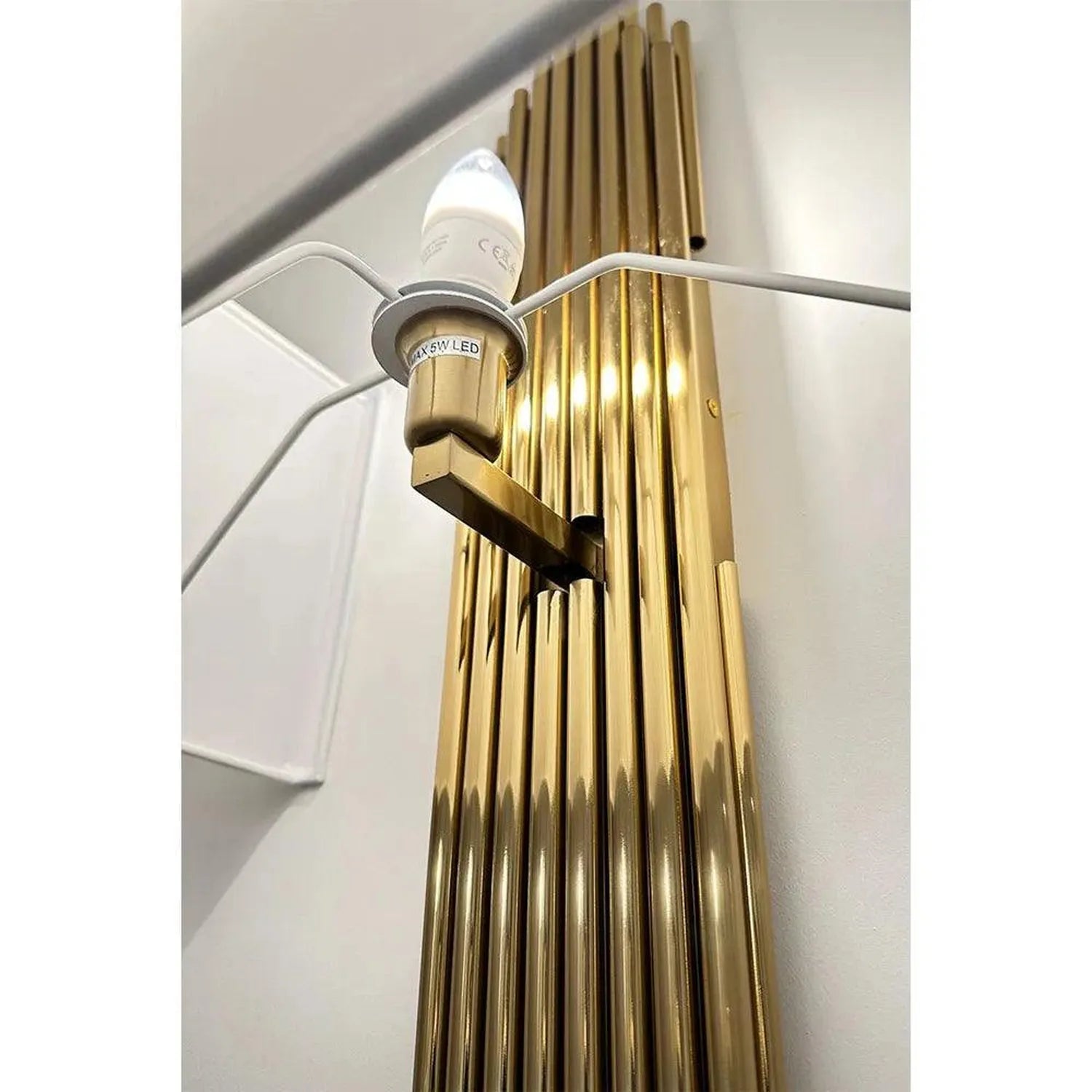 Gold ribbed wall sconce with white LED bulb installed, shown mounted on white wall.