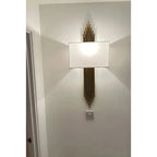 Gold vertical lined wall light with rectangular white shade mounted on white wall in modern interior setting.