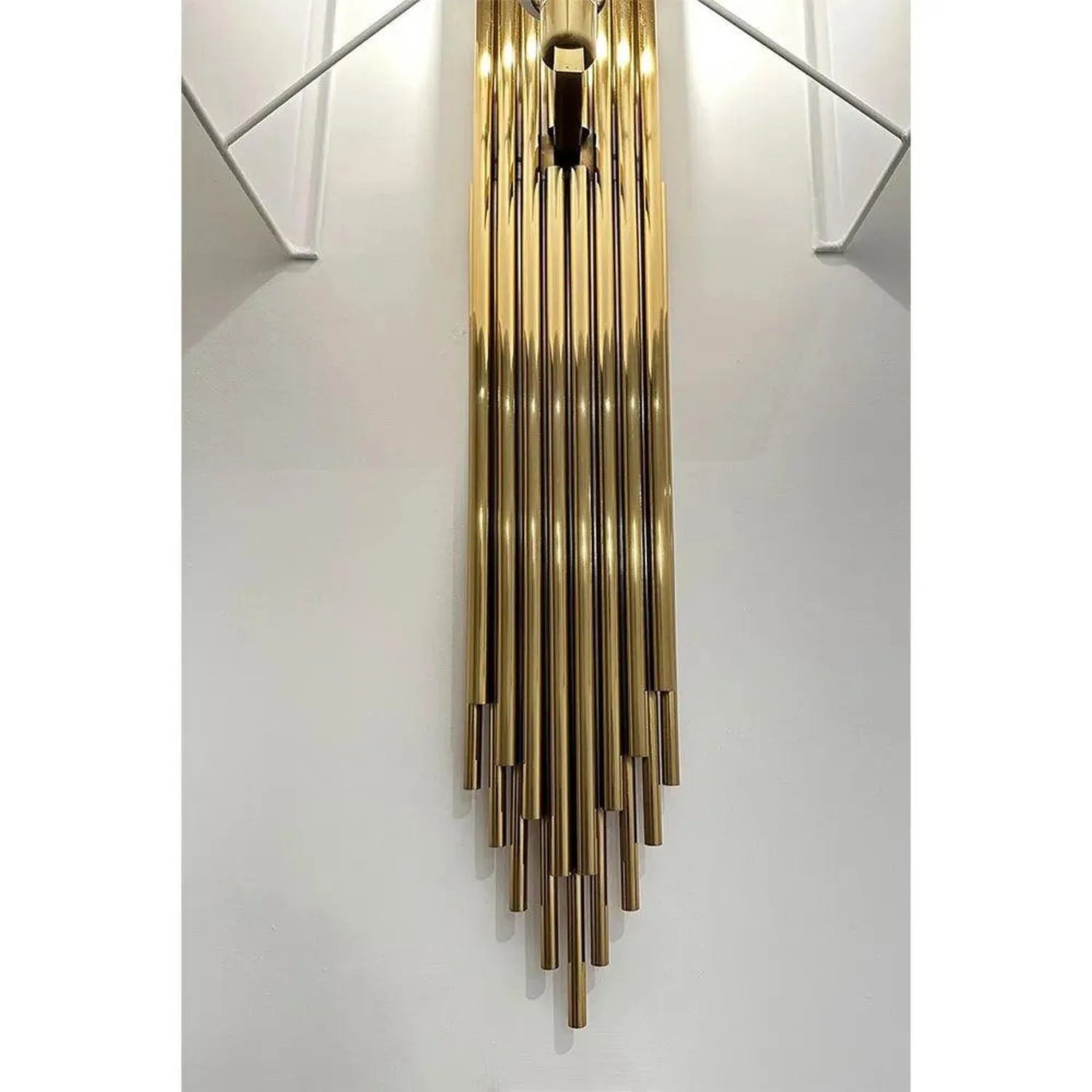 Gold tubular pendant chandelier with cascading rods hanging in white stairwell, installation shot.
