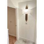 Gold finish wall sconce with rectangular linen shade installed above wall outlet in contemporary hallway.