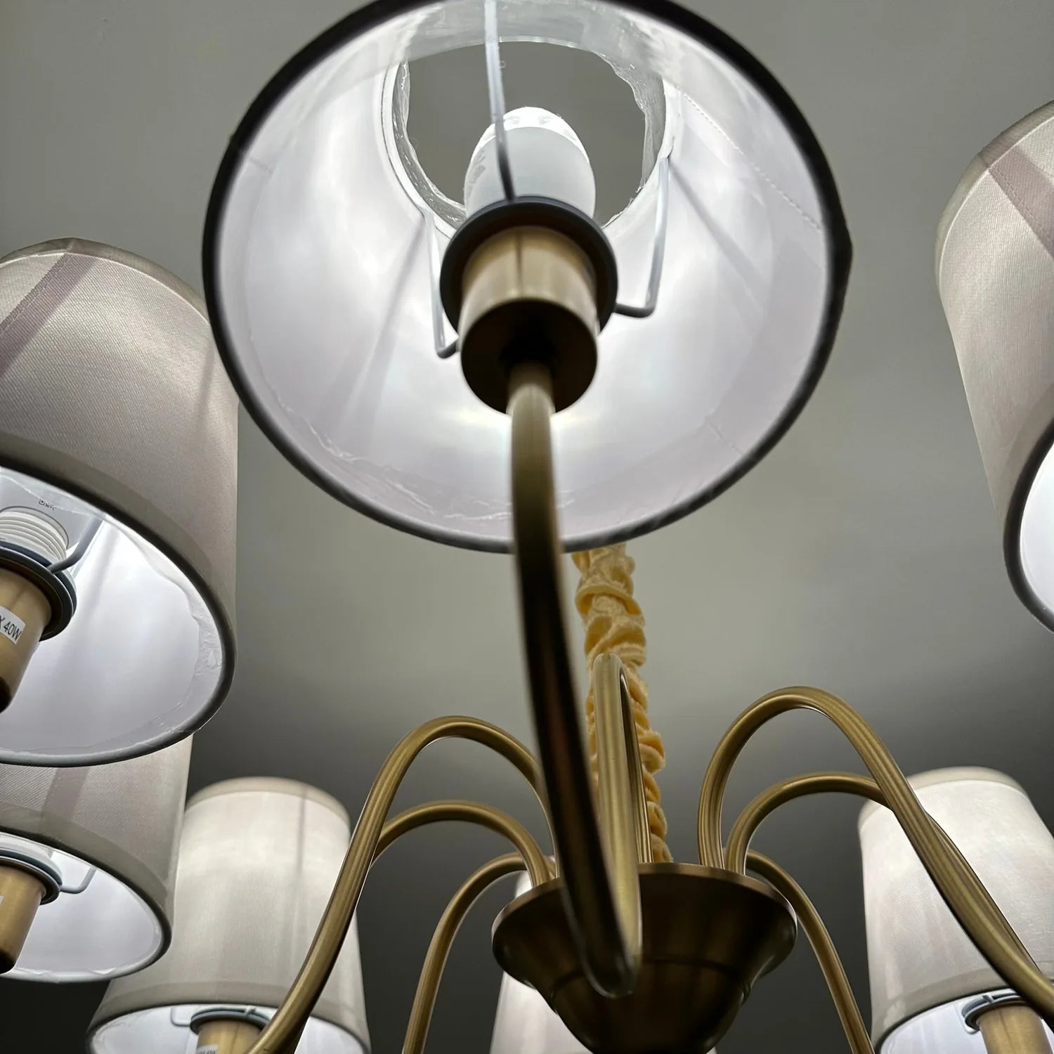Aurelia Gold 8 Light Chandelier viewed from below, showing brass arms with white fabric shades and central stem against ceili