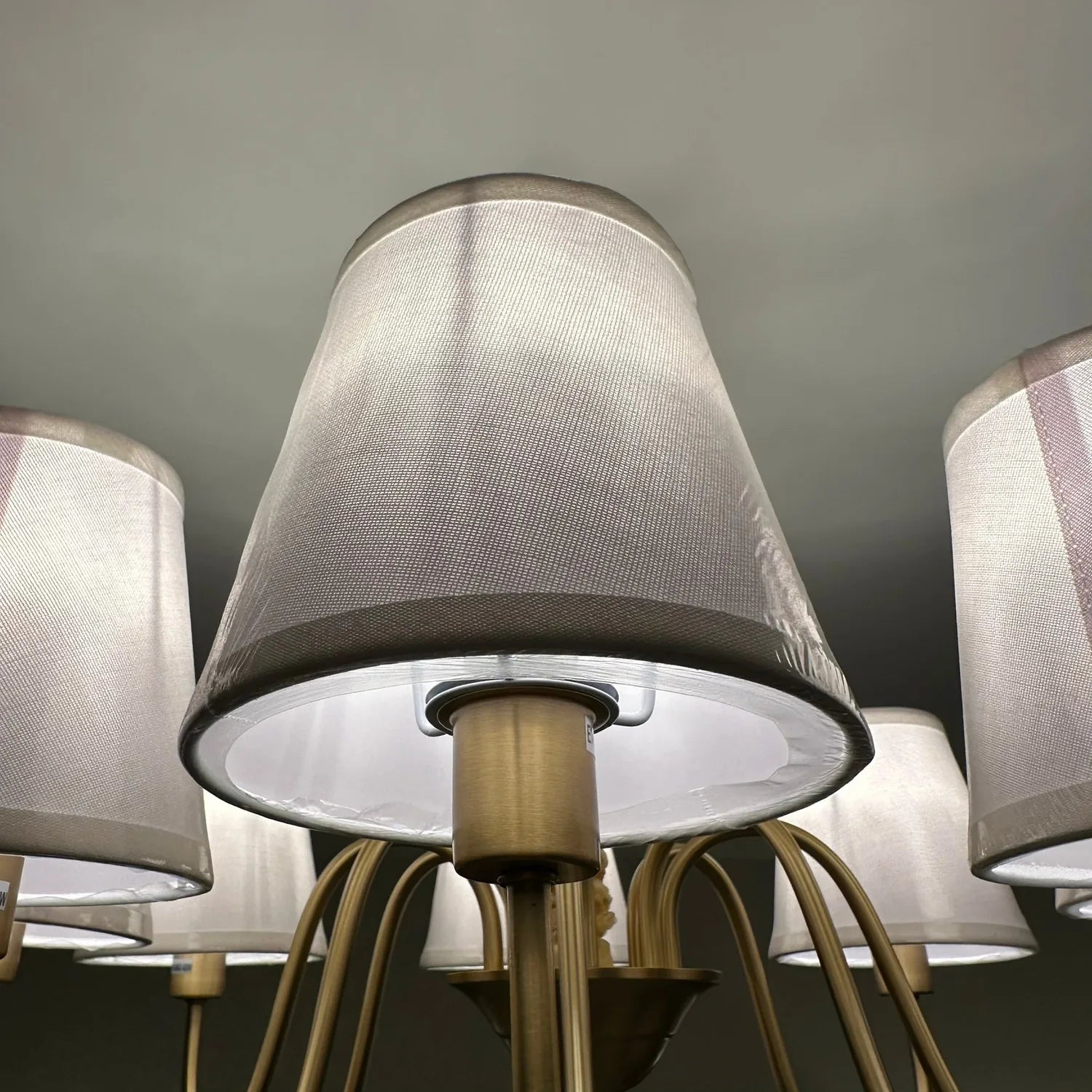 Aurelia Gold 8 Light Chandelier with white fabric drum shades and brass arms mounted on ceiling, installation shot.