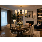 Aurelia gold eight-light chandelier installed in elegant dining room above dark table with cream upholstered chairs and firep