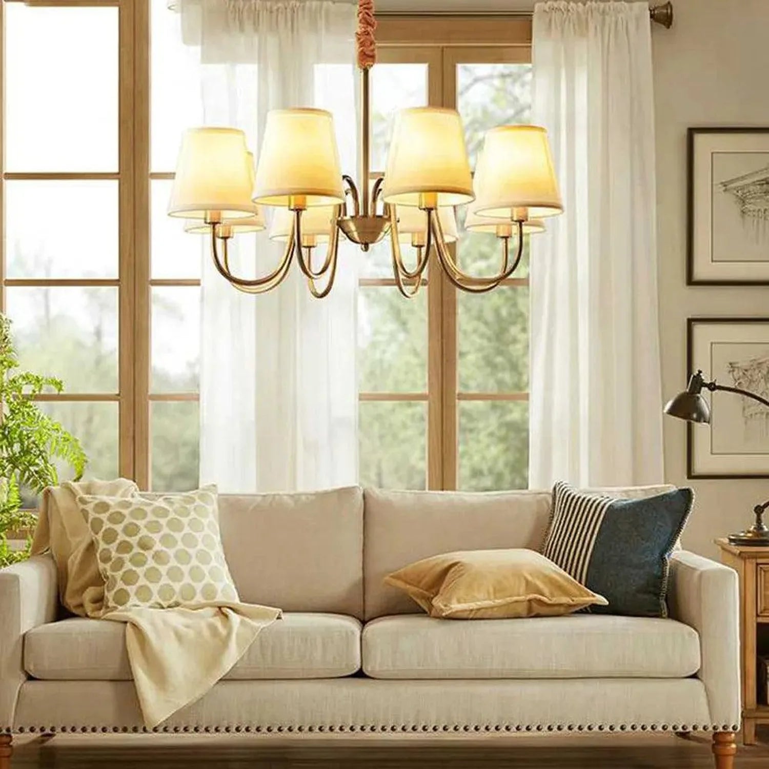 Aurelia gold eight-light chandelier hanging above beige sofa in bright living room with windows and sheer curtains.