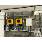 Off-grid solar installation in garage showing two yellow inverters, white battery management panel, and electrical wiring mou