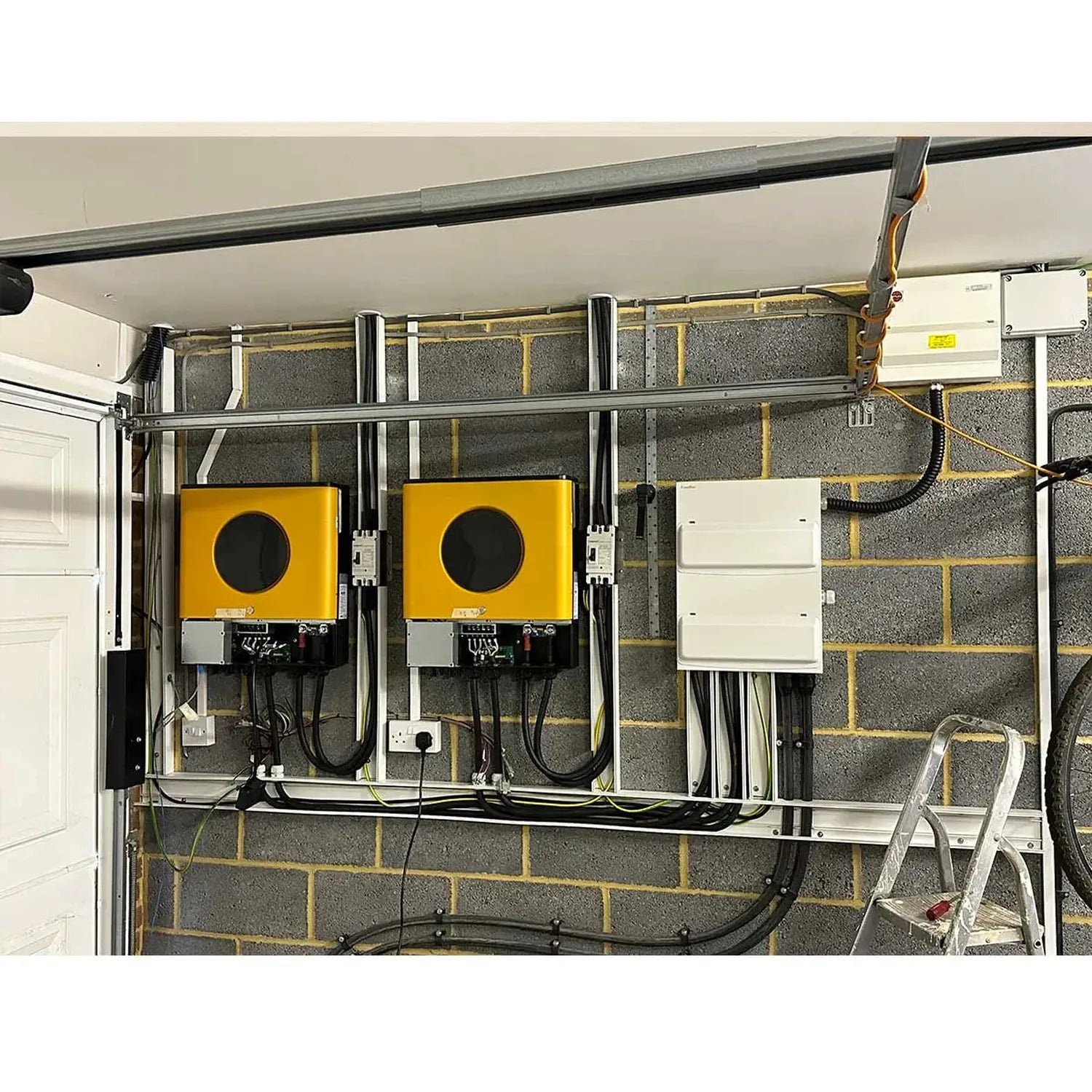 Off-grid solar installation in garage showing two yellow inverters, white battery management panel, and electrical wiring mou