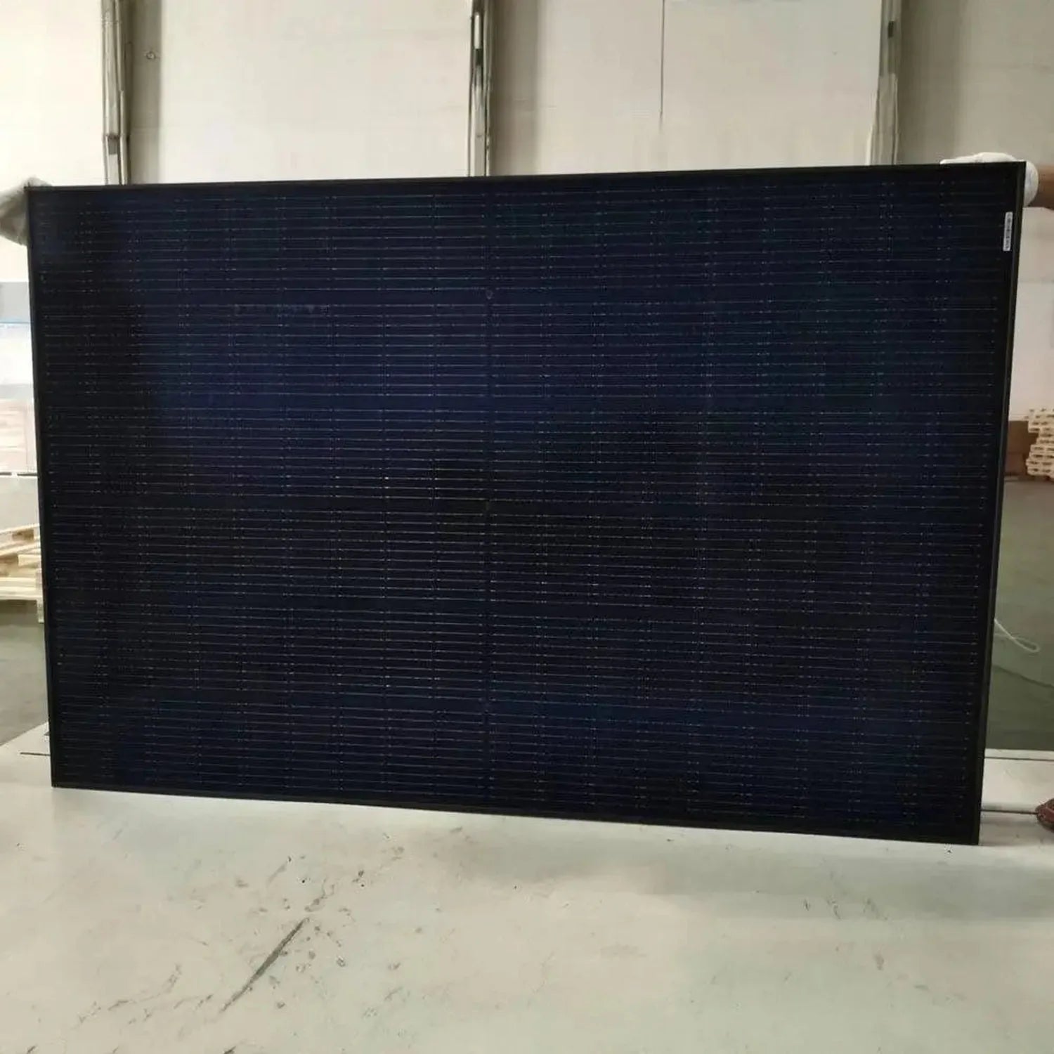 Black monocrystalline solar panel displayed on concrete floor indoors, showing grid pattern of cells.