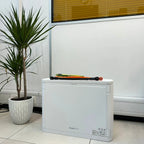 White Pylon Tech hybrid solar inverter displayed on desk with colored cables on top, potted palm plant to the left, and windo