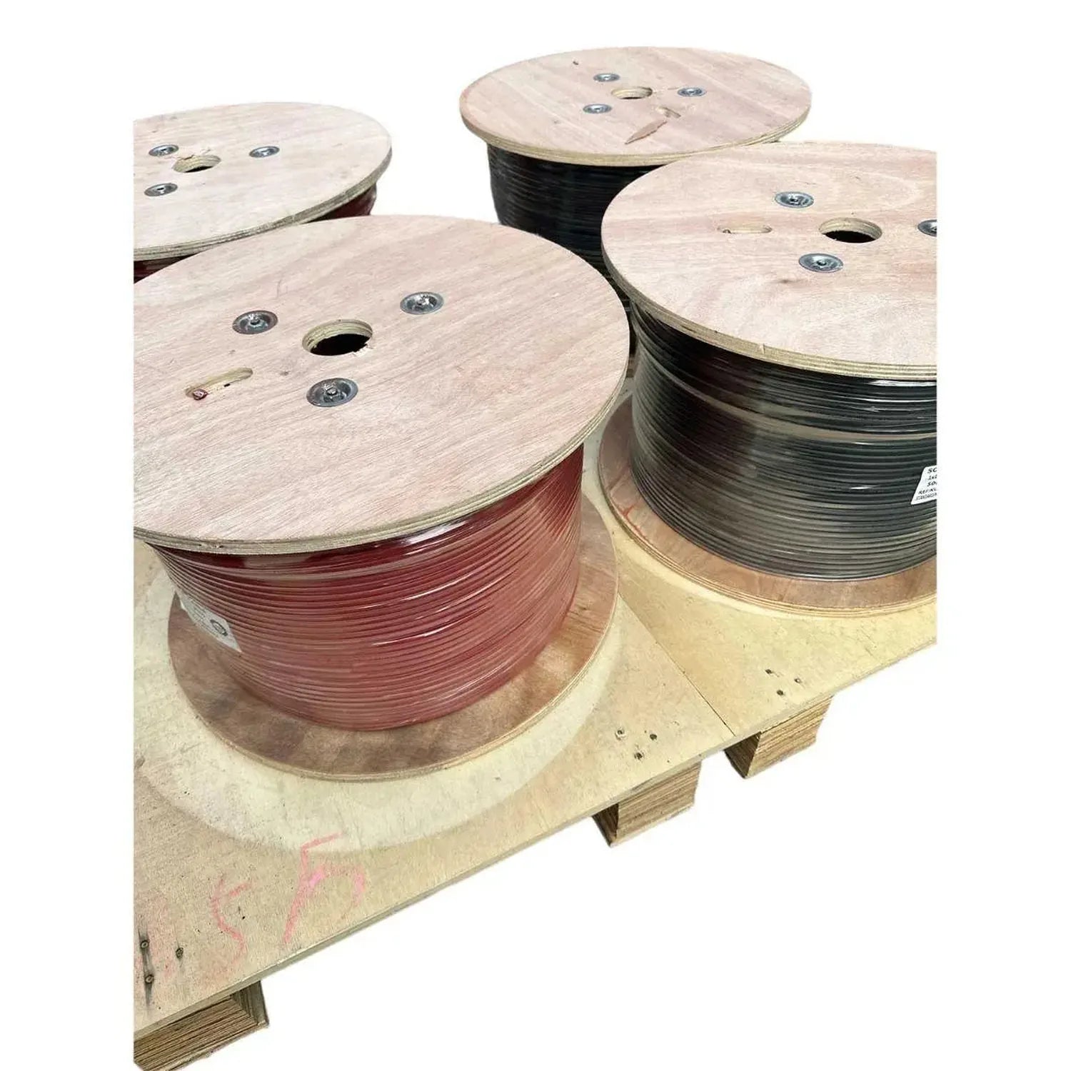 Four wooden cable drums with red and black coiled solar wire spools mounted on wooden pallets.