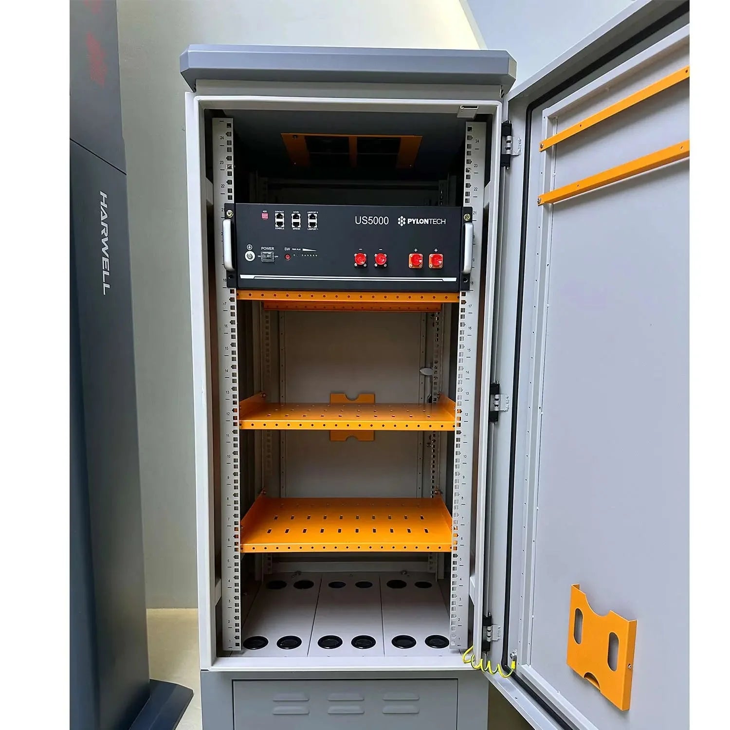 Pylontech US5000 battery enclosure cabinet with open door, showing three orange shelves and control panel with red switches m