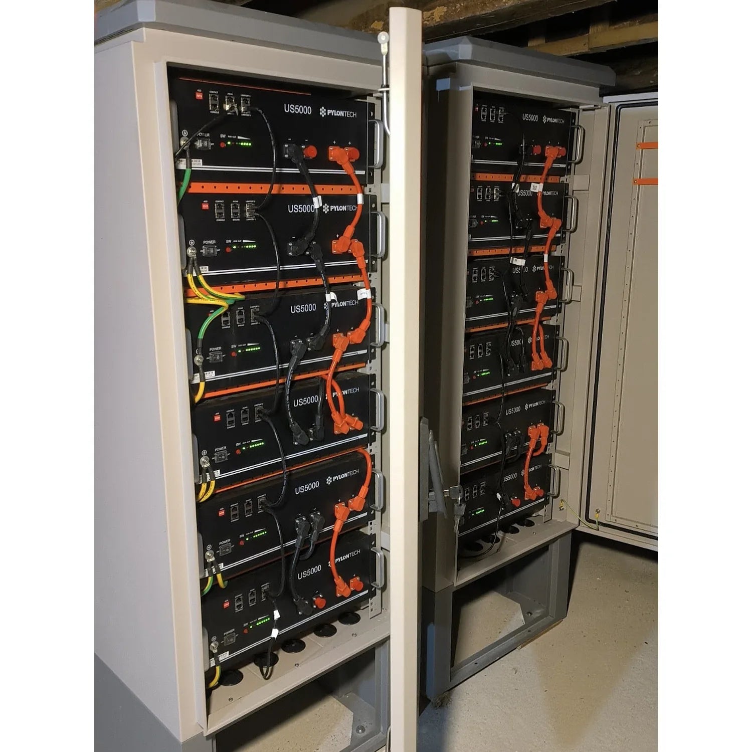 Stacked battery enclosure cabinet with six Pylontech US5000 units mounted vertically, orange and yellow cables visible, insta