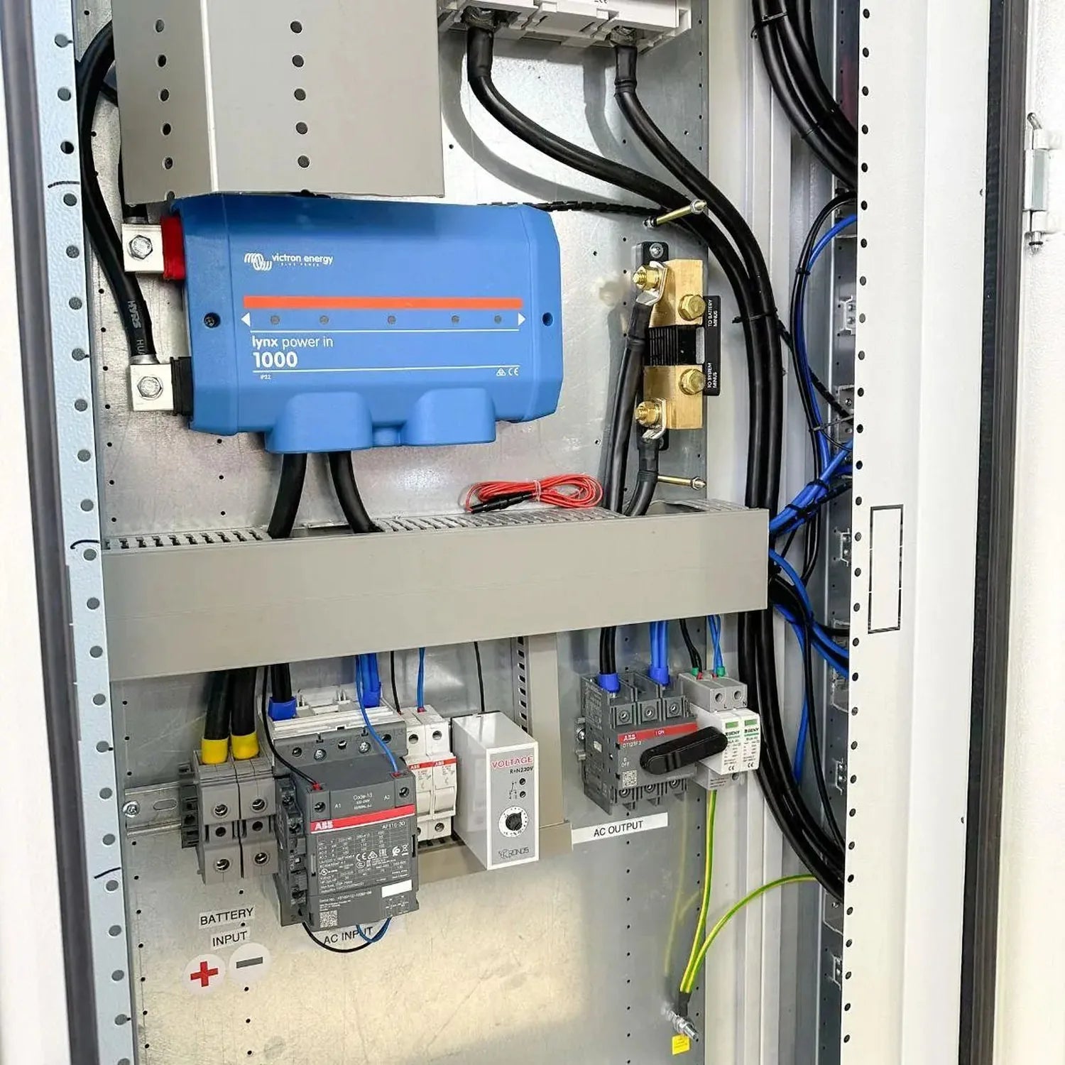 Interior installation view of floor-mounted power cabinet showing blue Victron Lynx Power In 1000 inverter, battery terminals