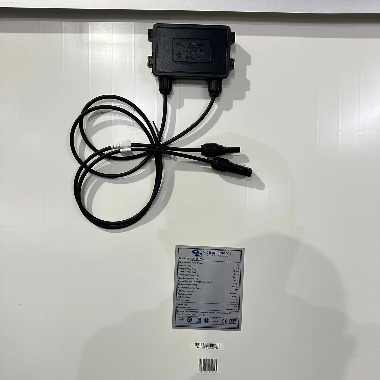 Black solar panel junction box with cables and Victron Energy specification label with barcodes on white surface.