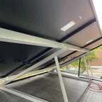 Solar panel installation on roof frame with white aluminum supports and black panel visible, showing mounting hardware and el