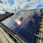 Rooftop installation of solar panels mounted on angled roof with antenna and brick chimney visible under partly cloudy sky.