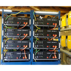 Eight Pylontech US5000 lithium batteries stacked in two blue metal racks with yellow and orange connectors in an industrial i