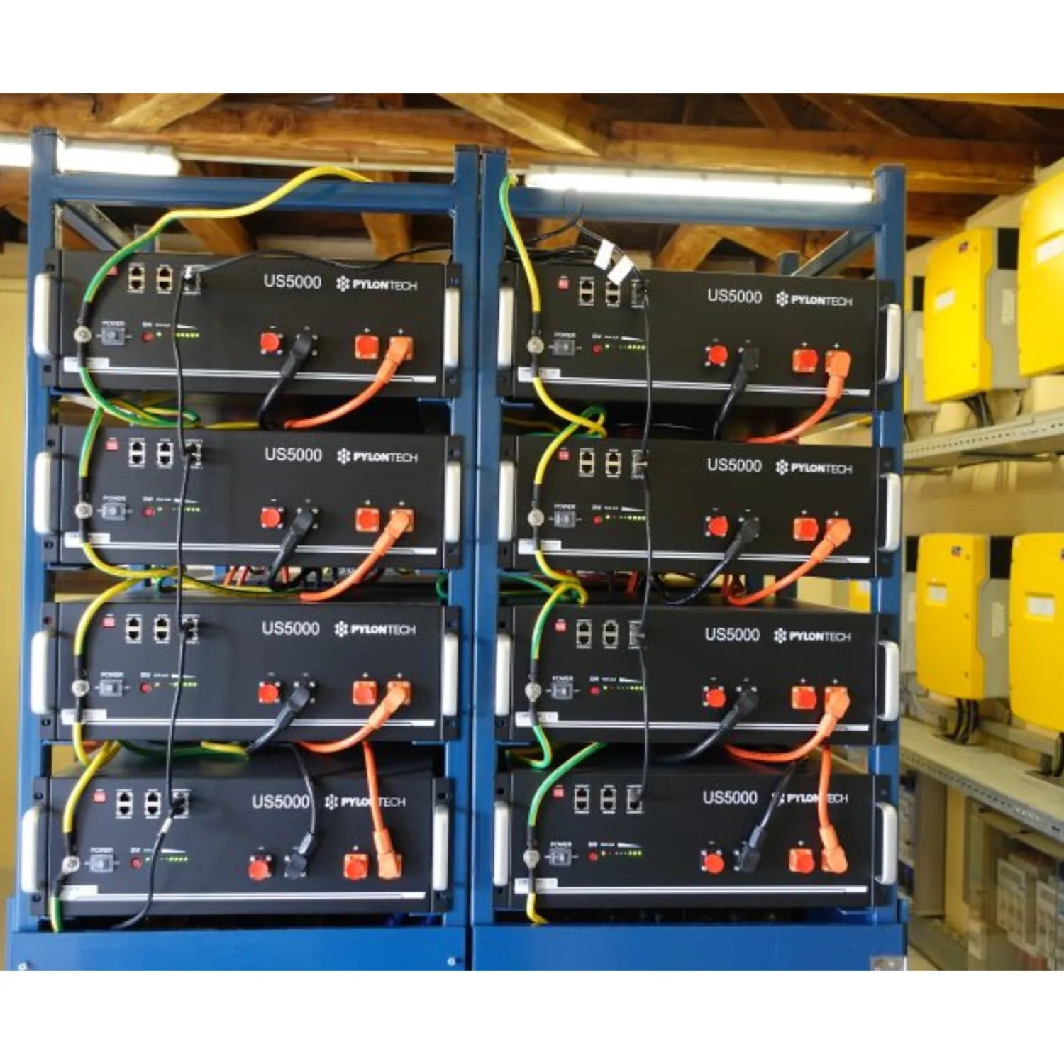 Eight Pylontech US5000 lithium batteries stacked in two blue metal racks with yellow and orange connectors in an industrial i