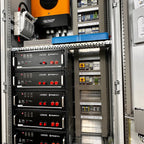 Industrial installation shot showing five stacked Pylontech US5000 battery units with red controls in a metal enclosure, alon