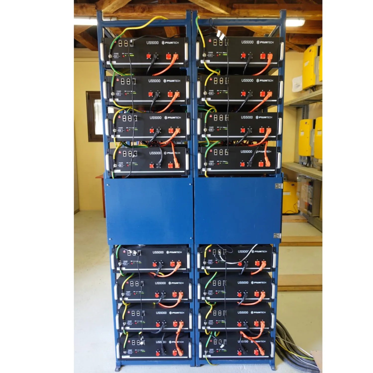 Two blue racks mounted with twelve Pylontech US5000 lithium ion batteries stacked vertically, connected with yellow and red c