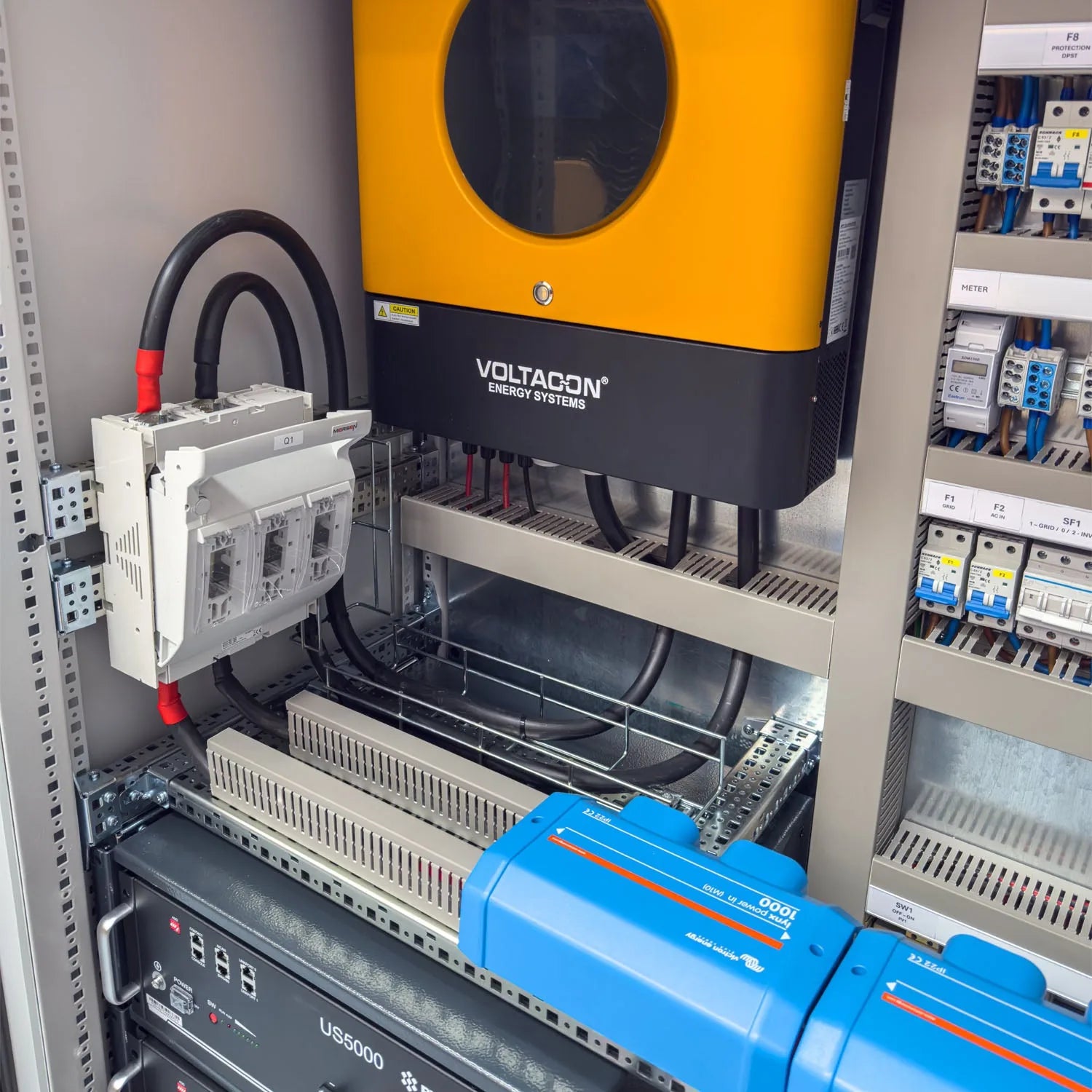 Voltacon energy systems cabinet installation showing yellow inverter, battery storage units, white controller, and electrical